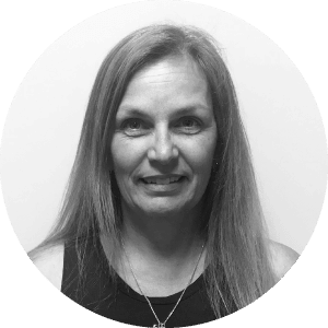 A portrait of a friendly, mature woman who represents the team behind Jonas Construction Accounting Software, exuding reliability and professionalism. The grayscale image set within a circular frame adds to the sleek and streamlined design of the software's website.
