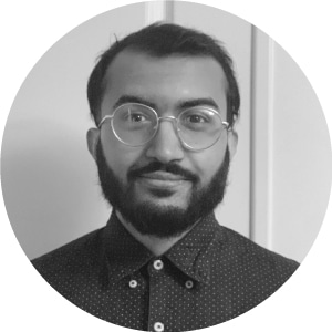 Portrait of a bearded man with round glasses and dotted shirt, smiling subtly in a plain office setting - typical of construction software industry workplaces.